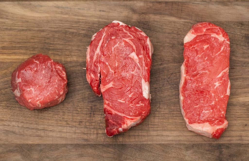 three different cuts of steak on a wood cutting board.