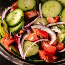 A cucumber, tomato, and onion salad in a clear glass bowl.