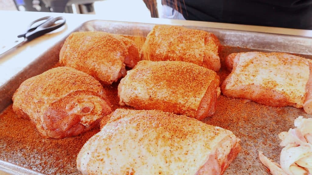 Seasoned chicken thighs on a large baking pan.