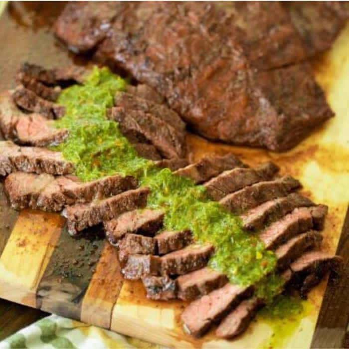 sliced grilled flap steak covered in chimichurri on a wooden cutting board