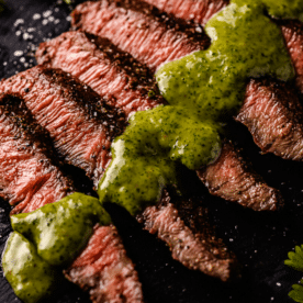 Sliced flap steak drizzled with cilantro chimichurri on a serving dish.