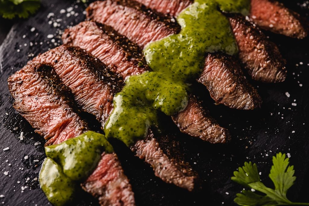 Sliced flap steak drizzled with cilantro chimichurri on a serving dish.