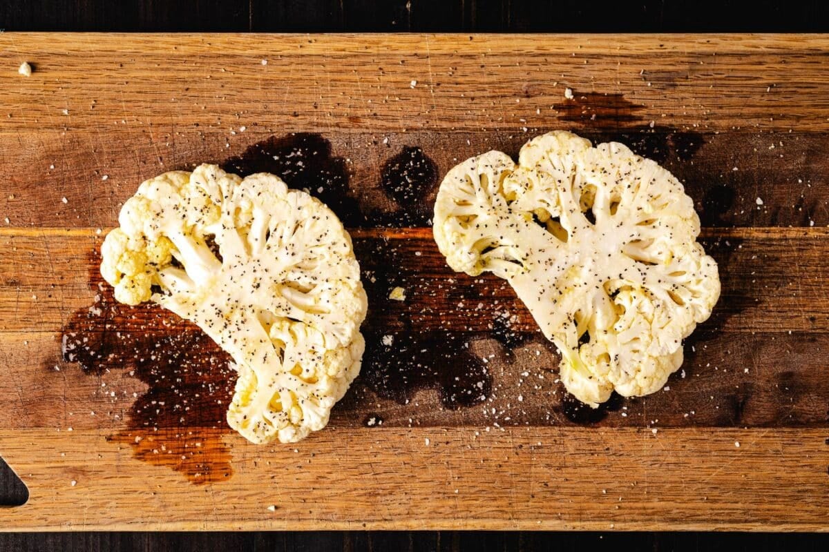 Cauliflower steaks on a cutting board drizzled with oil.