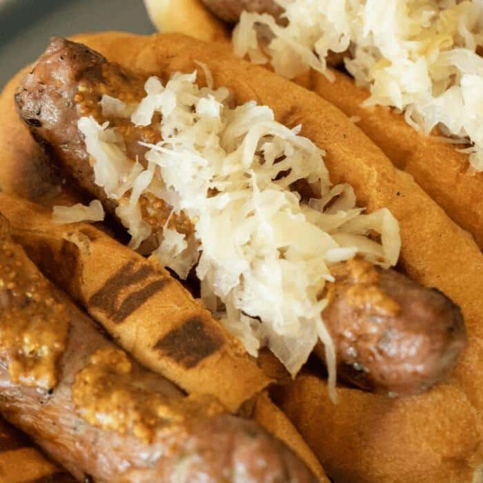 grilled bratwursts in buns topped with mustard and sauerkraut.