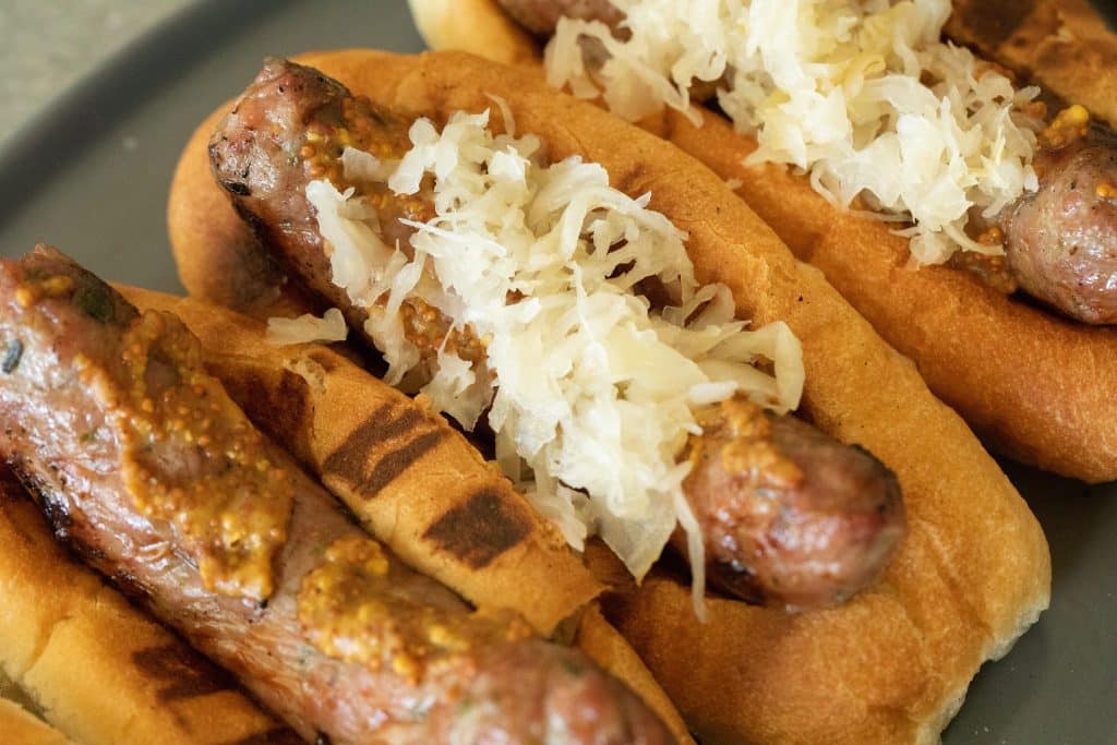 Grilled bratwurst in a bun with mustard and sauerkraut, overhead view displayed on a gray plate.