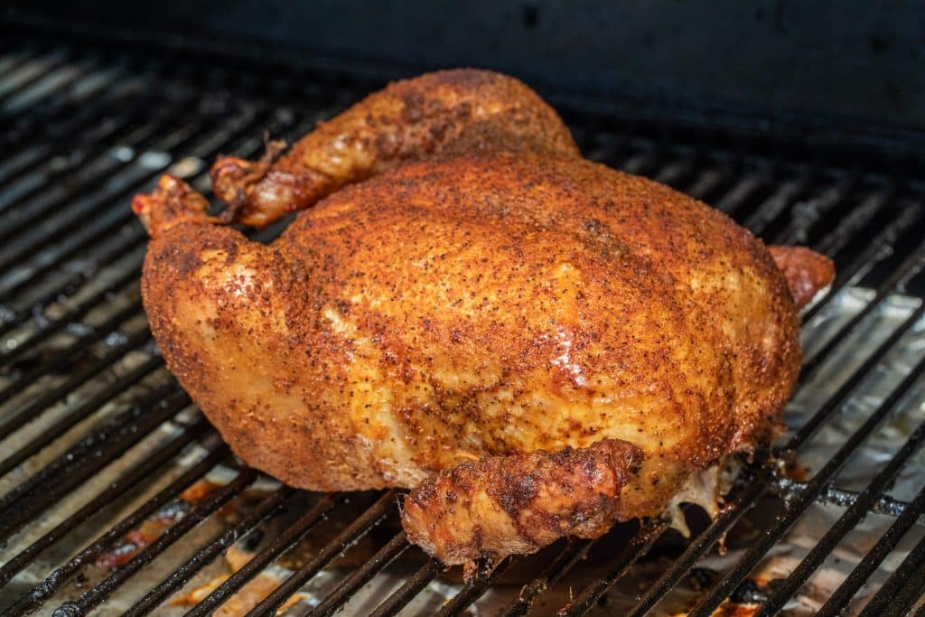 whole chicken coated in seasoning on a smoker.