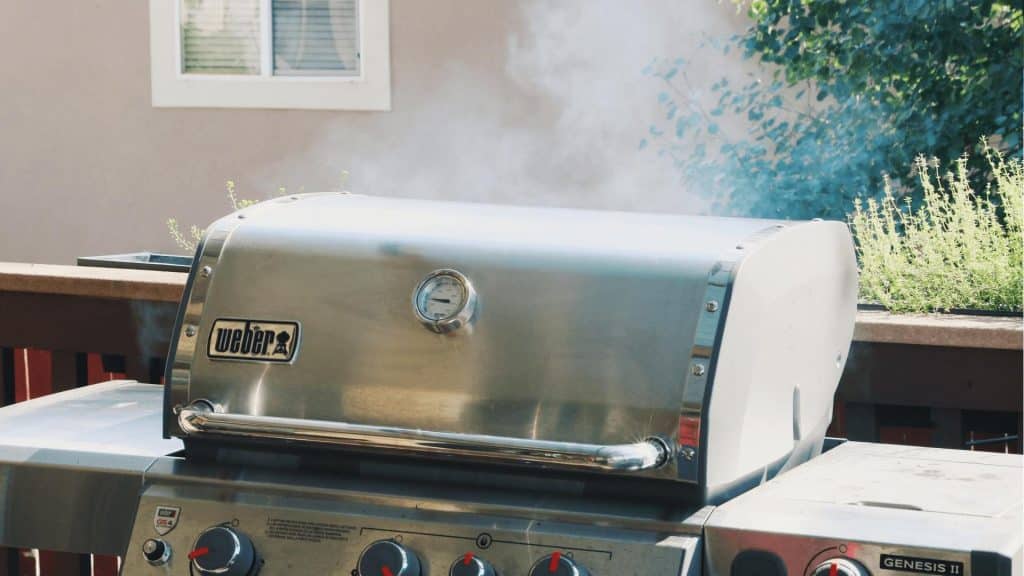 gas grill with smoke rising from the lid.