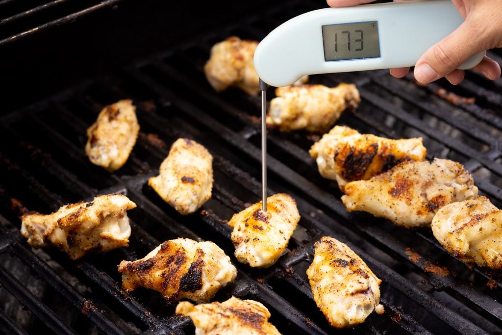 Instant read thermometer reading 173 degrees F in a chicken wing on the grill.
