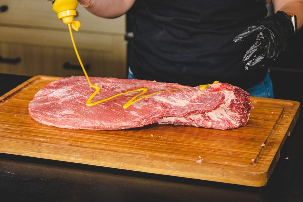 Yellow mustard being squirt on a brisket.