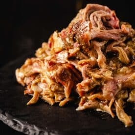 Shredded Chile verde pork piled on a round, black plate.