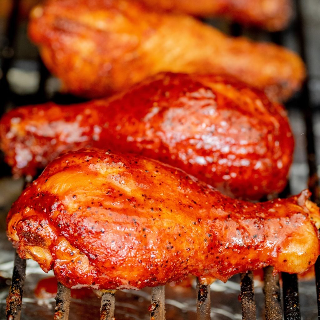 Four smoked chicken legs lined up on the grill grates of a pellet smoker.