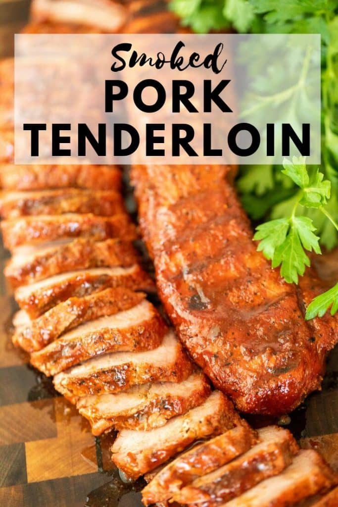 Sliced smoked pork tenderloin next to an unsliced pork tenderloin on a wood cutting board with green parsley.