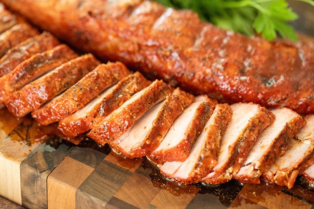 sliced smoked pork tenderloin on a wooden cutting board.