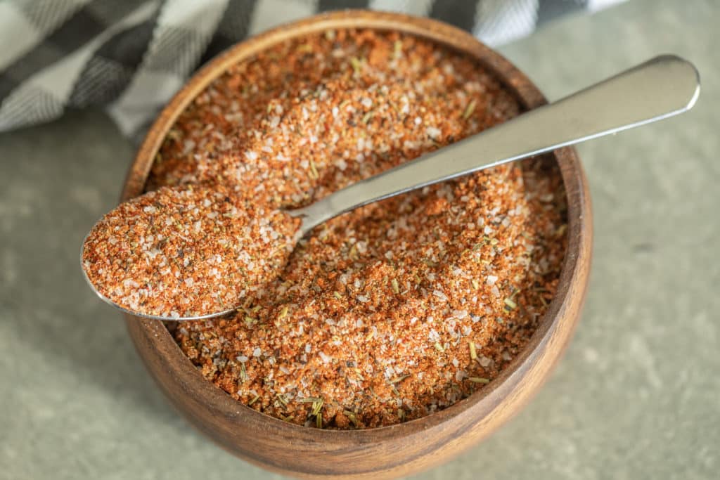 Spoonful of smoked turkey rub over a wooden bowl of smoked turkey rub.