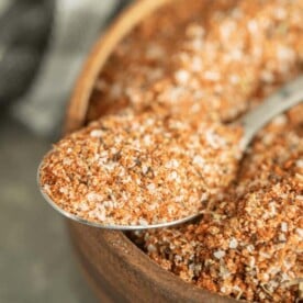 Spoonful of turkey rub resting on the edge of a wooden bowl full of the same rub.