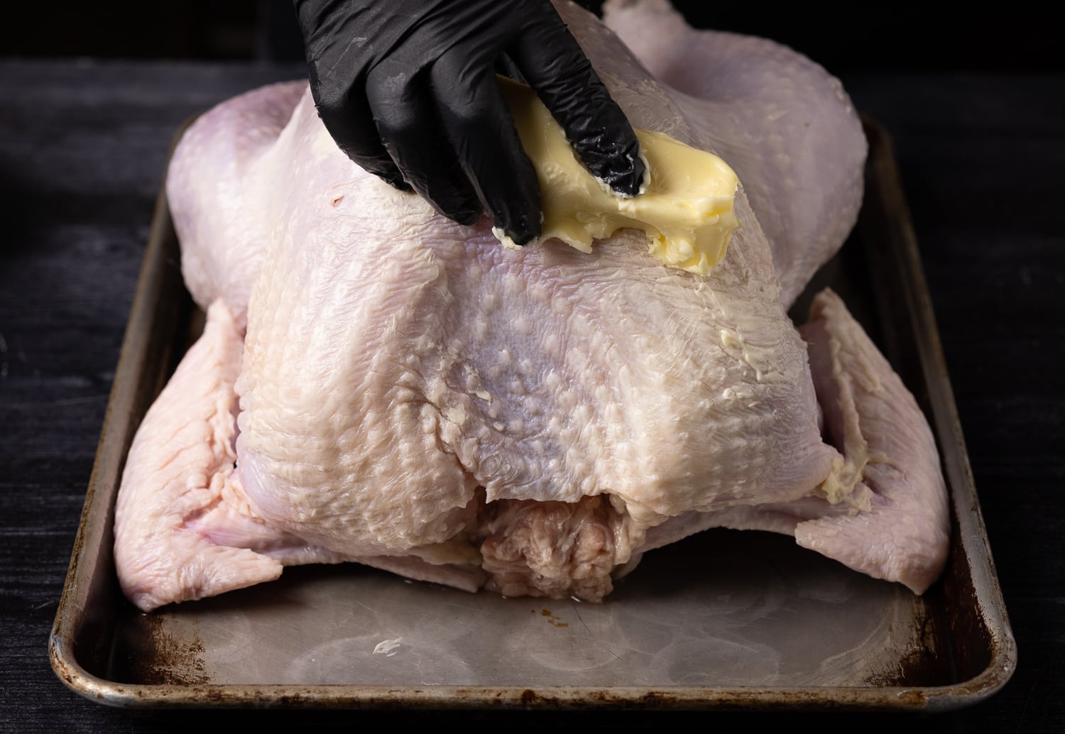 Butter being rubbed on the skin of a whole turkey.