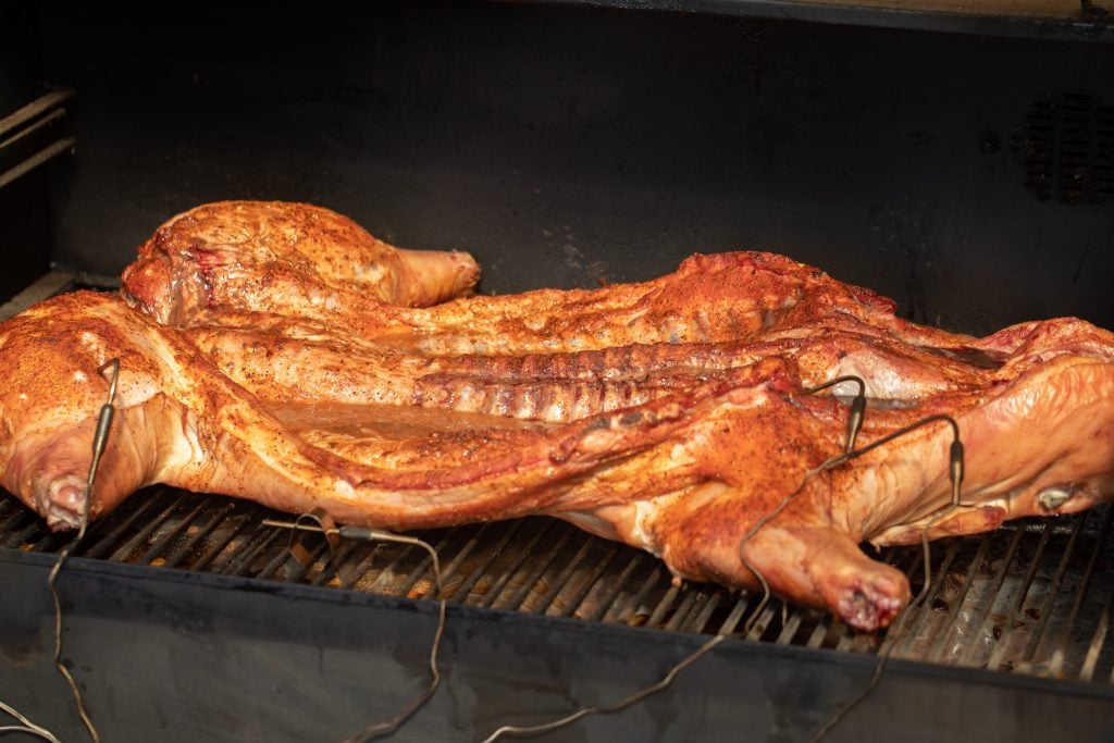 a whole seasoned pig that is laying flat on a smoker.