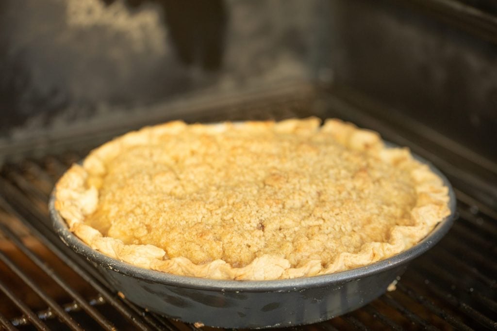 A partially cooked dutch apple pie on the grill grates in a smoker