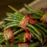 Bacon wrapped green bean bundles stacked on a metal baking dish.