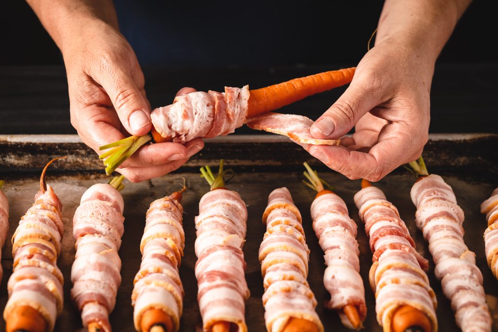 Carrots being wrapped in bacon.