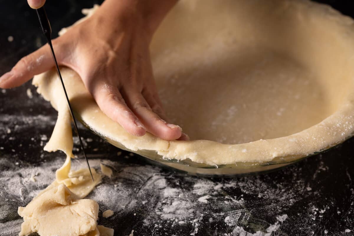 A chef's hand placing dough into a pie tin.