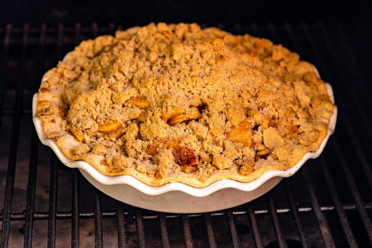 An apple pie cooking on the grates of a smoker.