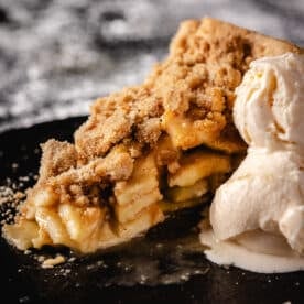 A slice of pie and a scoop of vanilla ice cream on a black plate.