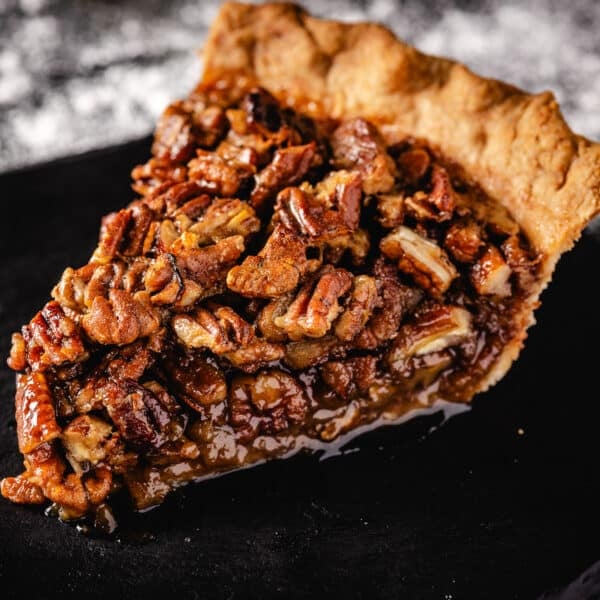 A slice of pecan pie on a black plate.