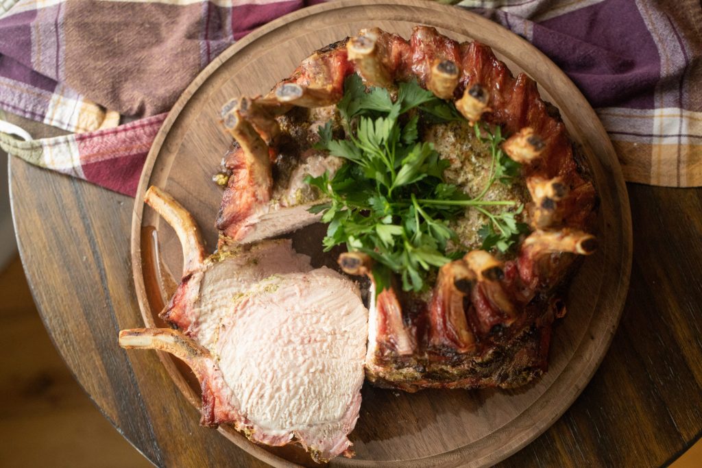 Overhead shot of a smoked pork crown roast on a wooden cutting board with two slices of the roast cut out and resting beside the roast.