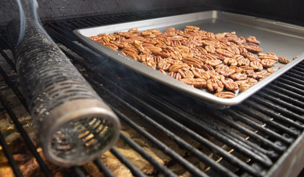 baking tray of pecans on the grill grates in a smoker next to a smoke tube.