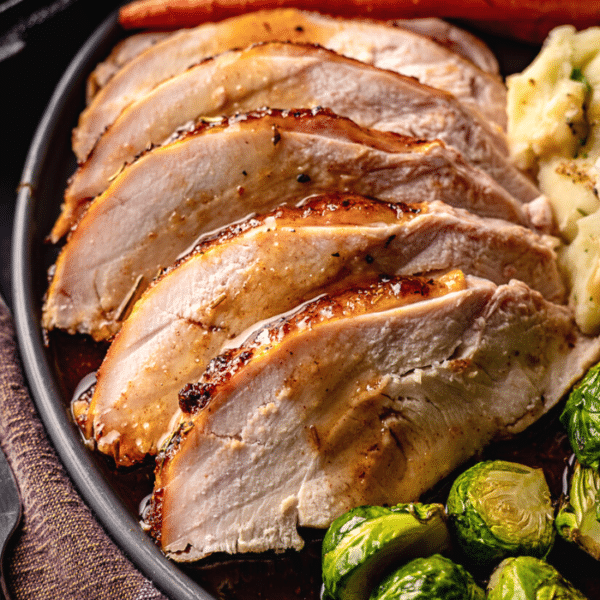 Sliced turkey breast on a plate next to brussels sprouts and mashed potatoes.
