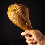 Hand holding a large smoked turkey leg.