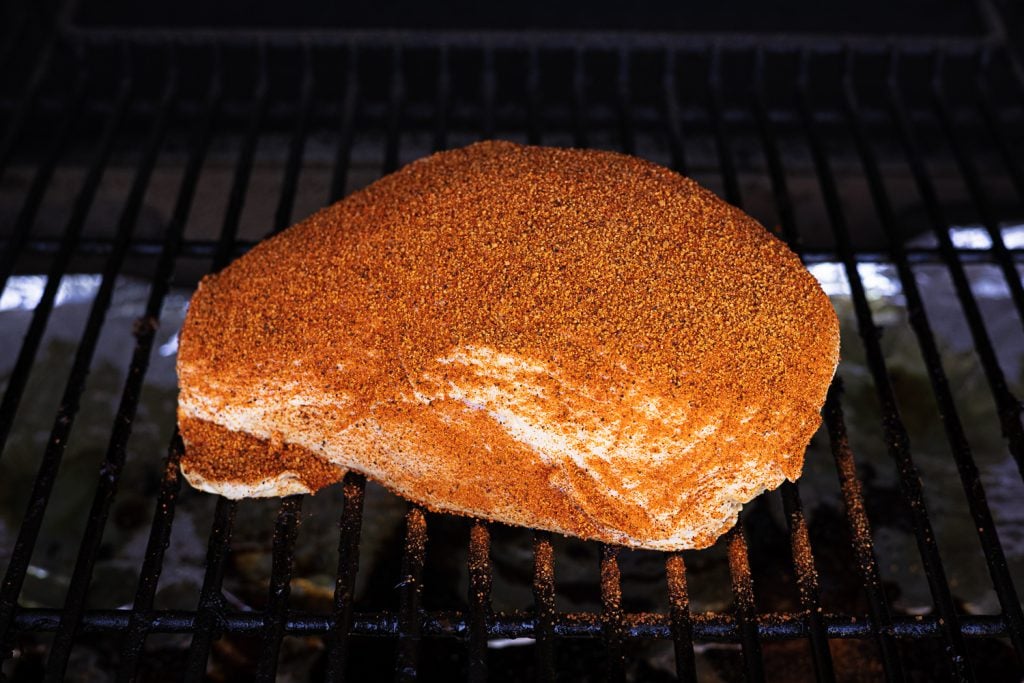 Seasoned turkey breast on the grill grates of a smoker.