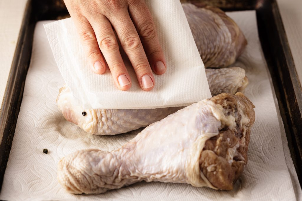 Brined turkey legs being pat dry with a paper towel.
