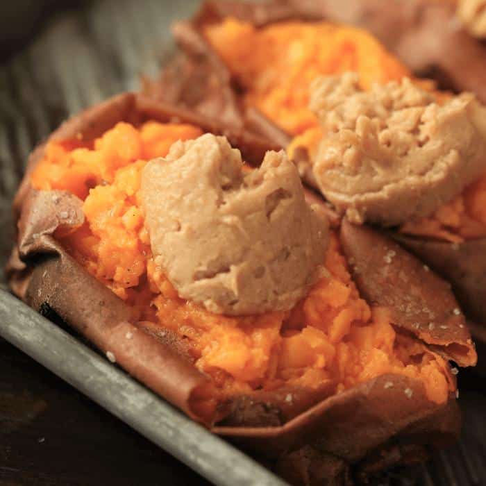 Two smoked sweet potatoes topped with maple cinnamon butter in a metal baking dish.