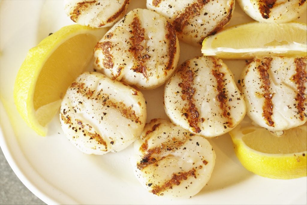 grilled scallops on a white serving plate with lemon wedges.