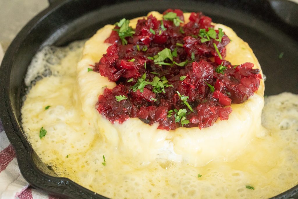 Grilled brie in a cast iron skillet that is all melty topped with cranberry jalapeno relish.