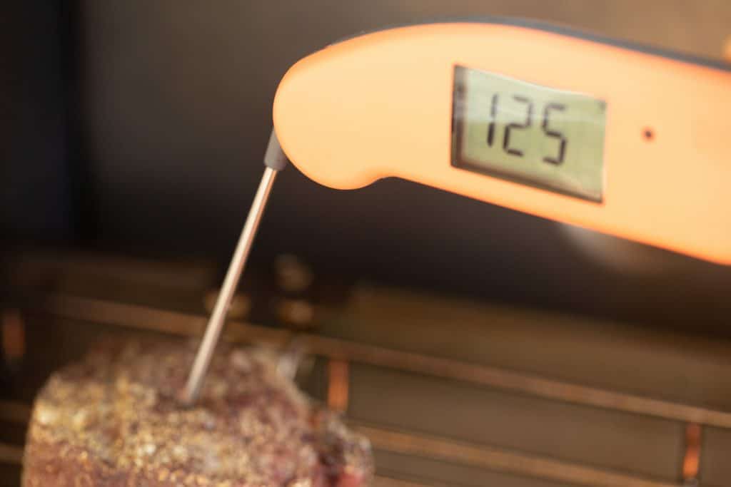 meat thermometer probe in a grilled filet mignon showing a temperature of 125 degrees F.
