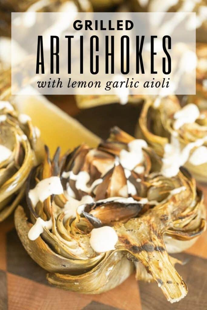 Grilled artichoke halves on a wooden board drizzled with lemon garlic aioli.