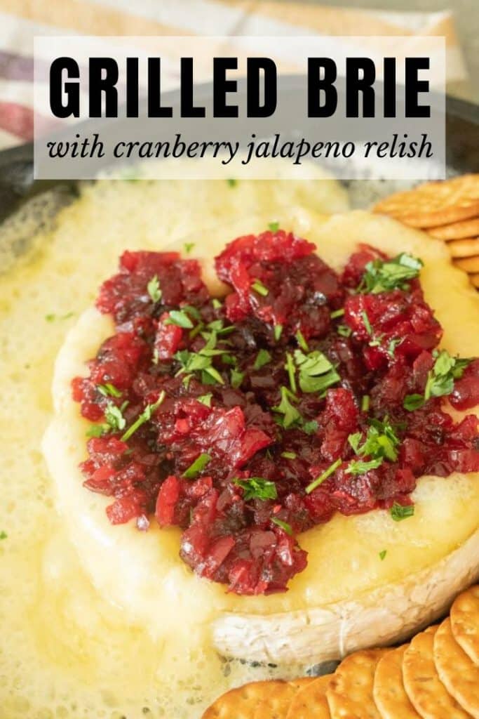 Grilled, melty brie topped with cranberry jalapeno relish next to whole grain crackers. Text overlay: Grilled Brie with Cranberry Jalapeno Relish.