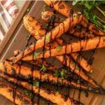 Grilled carrots drizzled with a balsamic glaze stacked on a wooden cutting board.