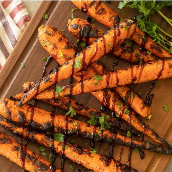 grilled carrots drizzled with balsamic glaze on top of a wooden cutting board
