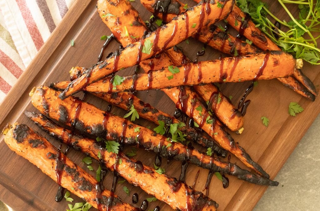 grilled carrots on a wooden cutting board drizzled with balsamic glaze.