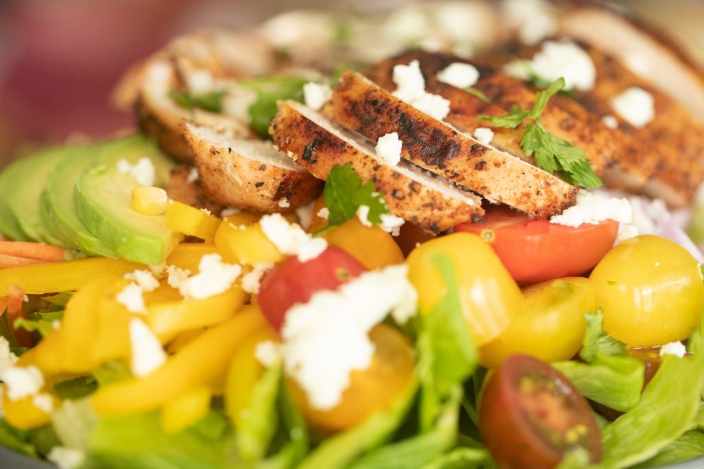 close-up image of grilled chicken on top of a bed of lettuce and vegetables.