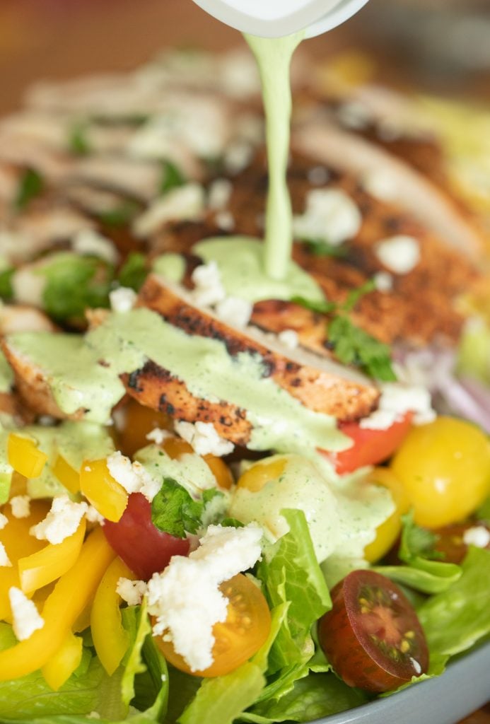 jalapeno lime salad dressing being poured on top of a grilled chicken salad.