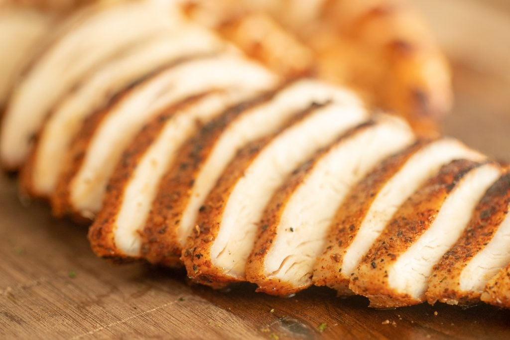 sliced grilled chicken for southwest grilled chicken salad on a wooden cutting board.