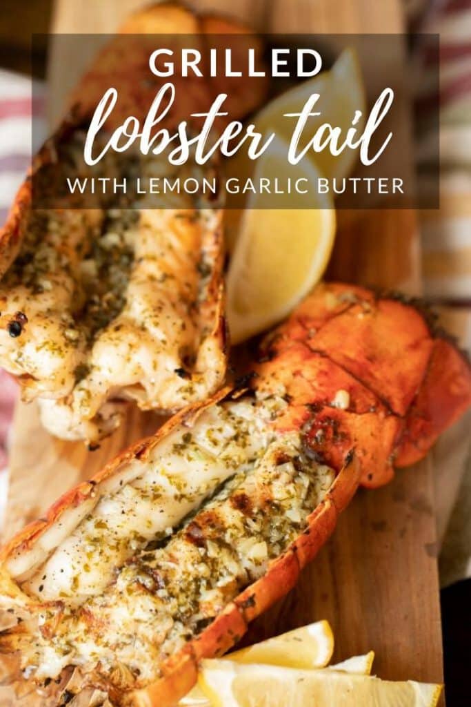 two grilled lobster tails on a wooden board with lemon wedges.