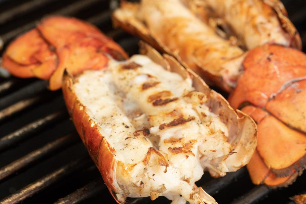 lobster tail halves split open on the grill.