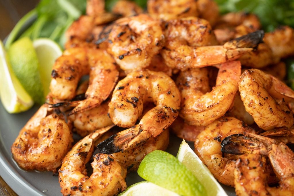 plate of seasoned and grilled shrimp with lime wedges.
