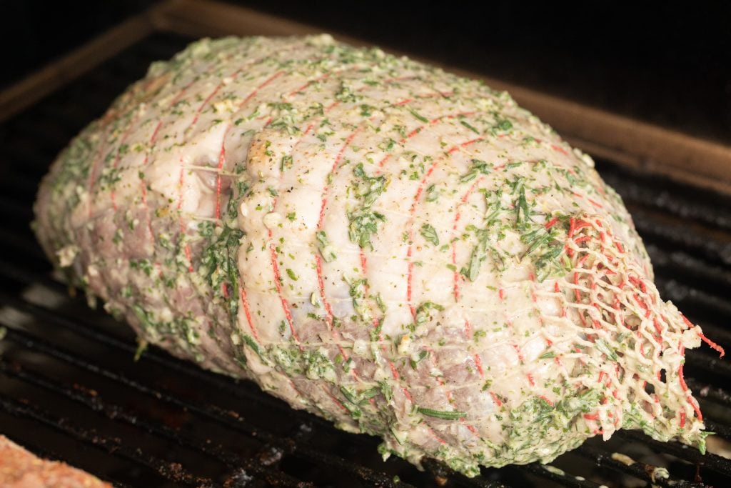 marinated leg of lamb on the grill grates of a smoker.